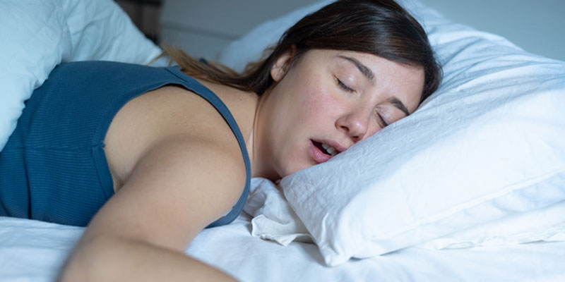 Woman sleeping on bed with mouth open in blue top.